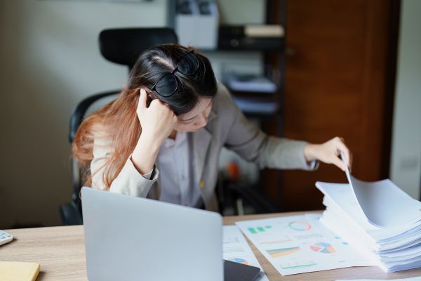 A distressed woman sifting through papers and checking through her laptop