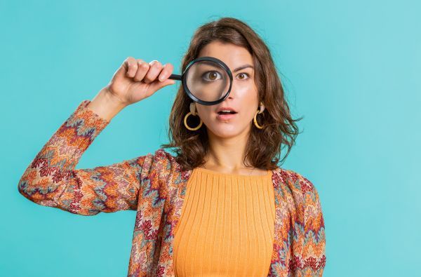 Woman looking through a magnify glass towards the camera