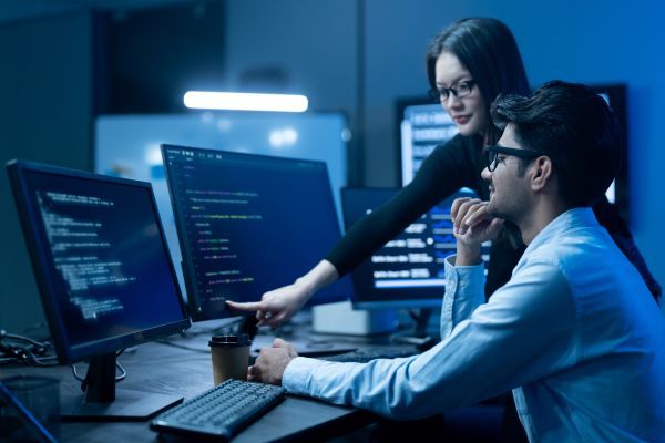 A manager helping a worker by pointing something out to them on a monitor.