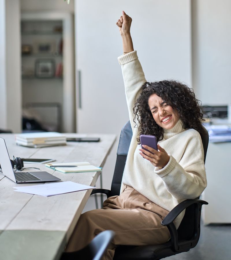 woman in an office expressing excitement while holding a mobile phone