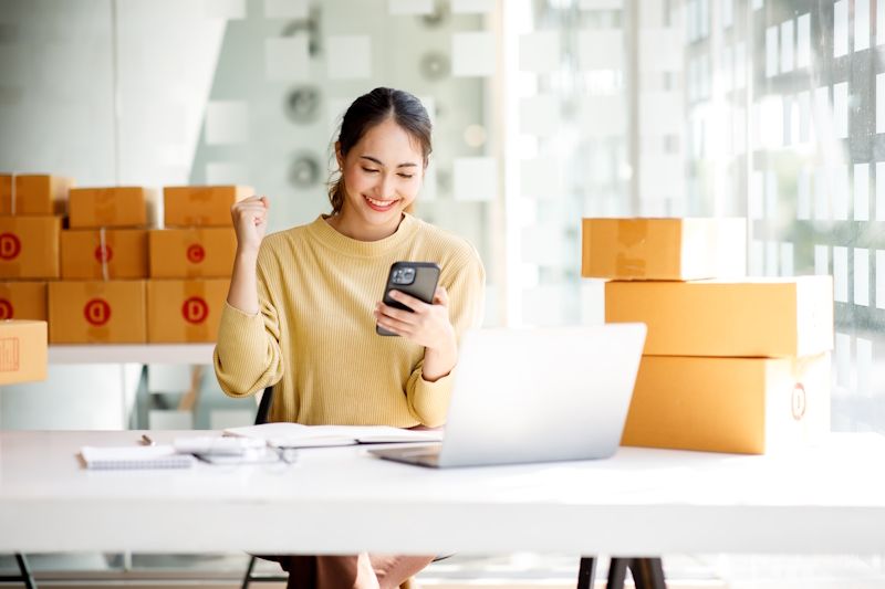 woman with shipping boxes shopping on a mobile phone